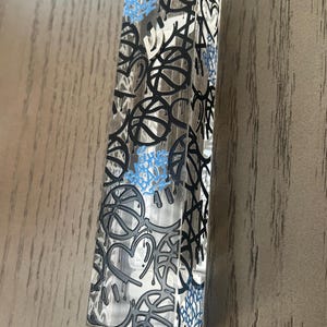 May include: A clear, rectangular object with a graffiti-style design featuring basketballs, hearts, and abstract shapes in black, gray, and light blue. The object is standing upright.