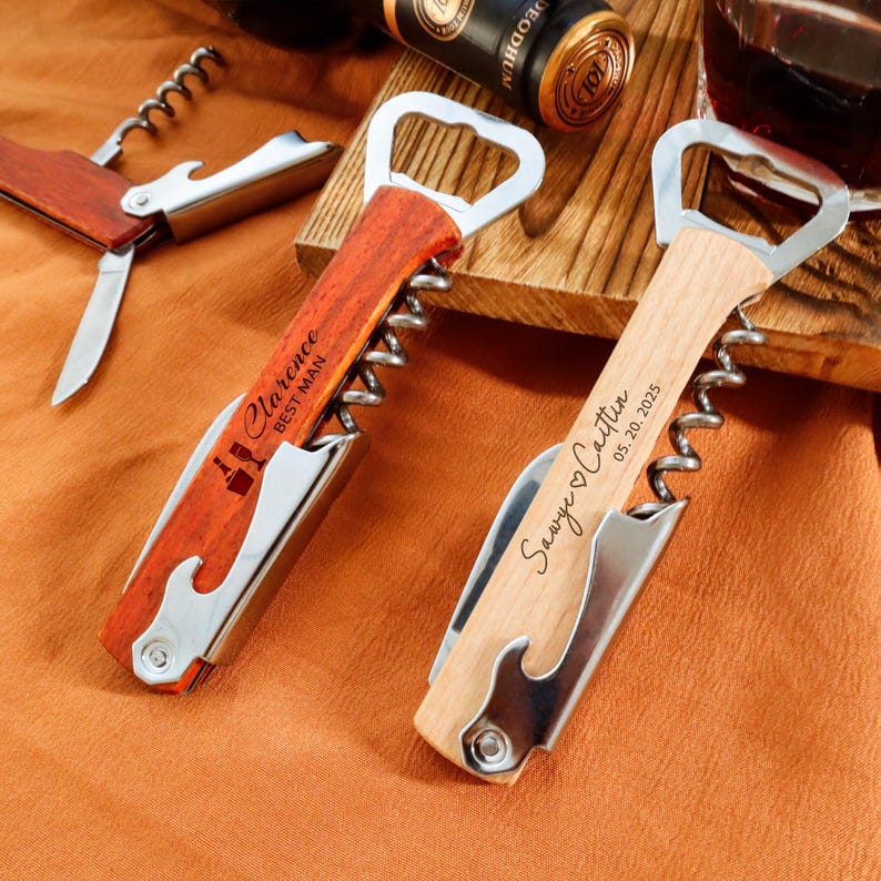 May include: Two personalized wooden bottle openers with corkscrews and bottle cap openers. One has "Clarence BEST MAN" engraved, the other "Sawye ♡ Caitlin 05.20.2025". A third wooden tool with a corkscrew and knife is also visible.