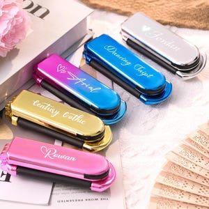 May include: A selection of personalised compact mirrors in shades of pink, gold, blue, and silver. Each mirror features a unique name or text engraving, such as "Rowan", "Arial", "Dancing Taipt", and "Jordan".