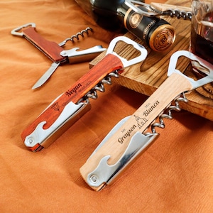 Könnte beinhalten: Holz-Korkenzieher mit Flaschenöffner und Messer. Auf einem Korkenzieher steht "Negan Groomsman 06.02.2025". Ein weiterer Korkenzieher trägt die Gravur "Mr. Grayson Mrs. Bianca" mit einer Kirchen-Ikone.