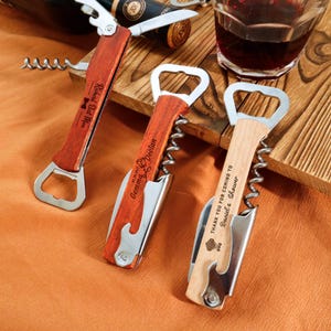 May include: Three personalized wooden wine opener tools with bottle opener and corkscrew features. One tool has the text "Richard Best Man", another "Gemma Declan", and the third "THANK YOU FOR COMING TO Daniel's Shower".