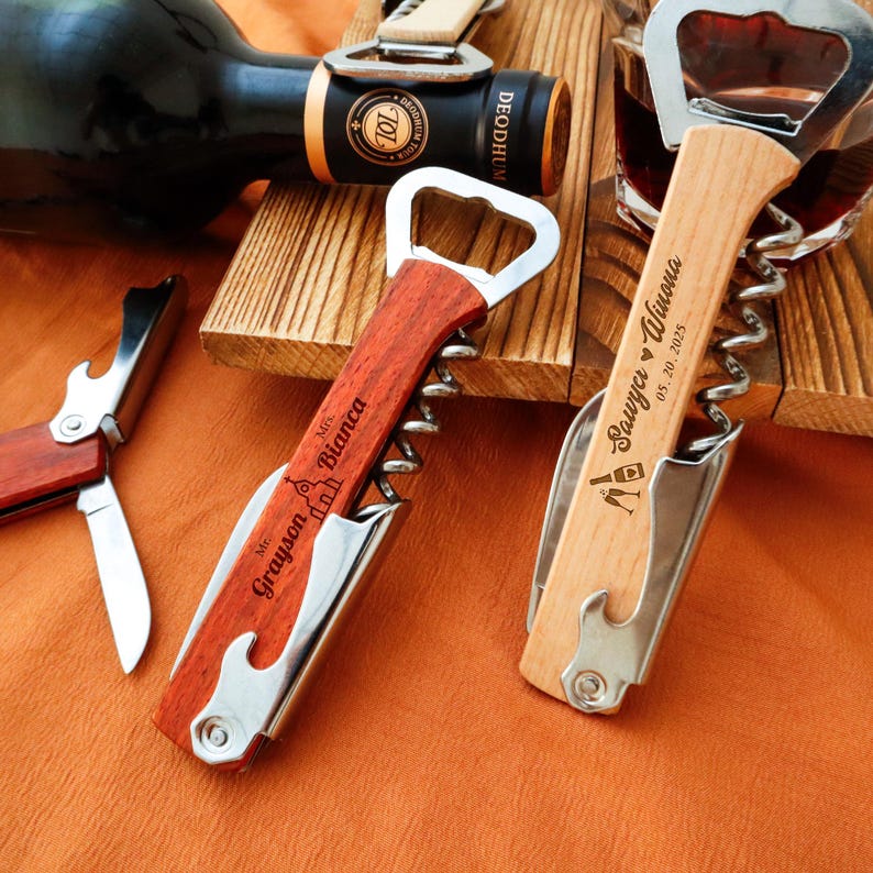 May include: Two personalized wooden wine bottle openers with silver accents. One is dark wood with "Mr. Grayson Bianca" engraved. The other is light wood with "Sawyer Winona 05.20.2025" engraved. A wine bottle and glass are in the background.