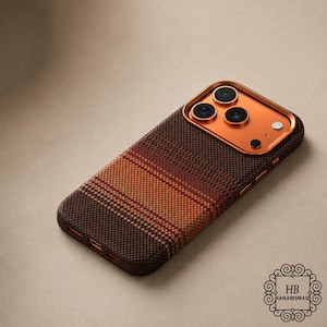 Puede incluir: Una funda de teléfono con un patrón de cuadros en tonos marrones, naranjas y rojos. El área de la cámara es de color cobre. La funda tiene un aspecto texturizado y una forma redondeada. El logotipo "HB HANABISMAID" está en la esquina inferior derecha.
