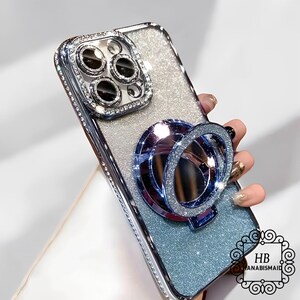 May include: A silver glitter phone case with a clear, multi-lens camera cover and a blue ring holder. The case has a sparkly, iridescent finish.
