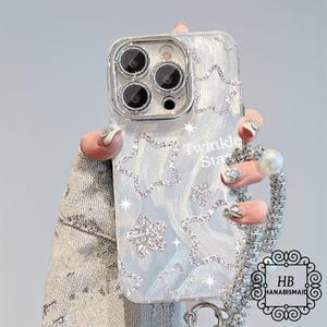 May include: A white iPhone case with a sparkly silver design and the words "Twinkle Star" printed on it. The case has a clear back and a silver trim. It is attached to a silver chain with a pearl charm.