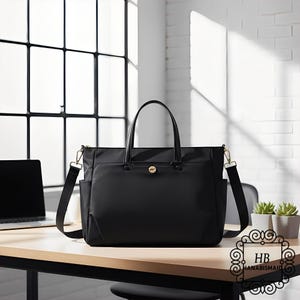 Könnte beinhalten: Eine schwarze Tragetasche mit einem oberen Griff und einem abnehmbaren Schultergurt. Die Tasche hat einen goldfarbenen Verschluss und Reißverschlussbeschläge. Die Tasche steht auf einem Holztisch neben einem Laptop.