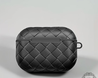 May include: Black woven AirPods Pro case. The case has a textured, basket-weave design. The case is oval-shaped with a small loop on the side. The case is made of a durable material and is designed to protect the AirPods Pro.