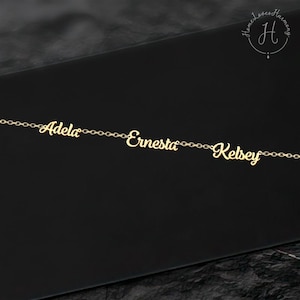 May include: A gold-colored metal chain necklace featuring three distinct nameplates in a cursive script font. The names Adela, Ernesta, and Kelsey are integrated into the chain links, creating a continuous horizontal design with a polished finish.