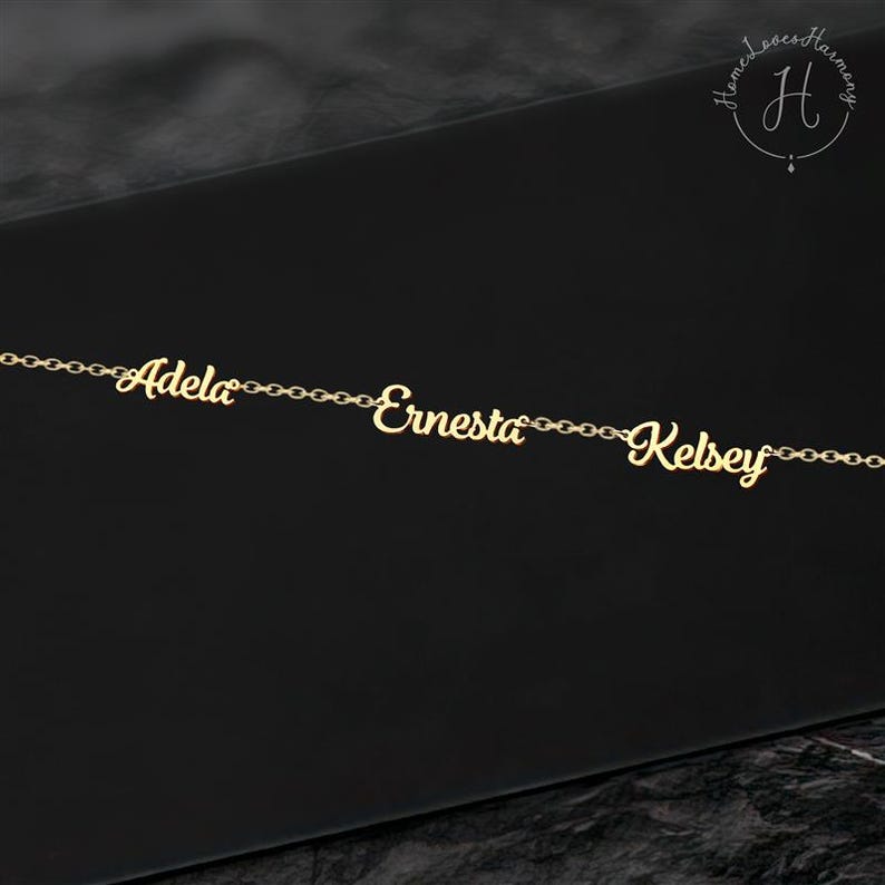 May include: A gold-colored metal chain necklace featuring three distinct nameplates in a cursive script font. The names Adela, Ernesta, and Kelsey are integrated into the chain links, creating a continuous horizontal design with a polished finish.