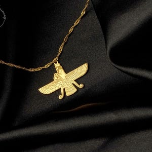 May include: A gold-coloured necklace featuring a Faravahar pendant with detailed wings and a central figure. The pendant hangs from a delicate twisted chain. A circular logo with the text Home Loves Harmony is visible in the upper left corner.