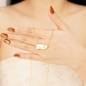 May include: A gold-toned necklace featuring a pendant shaped like the map of Puerto Rico. The pendant includes a small heart cutout and the engraved text Custom Name. The piece is suspended from a delicate gold-toned chain with twisted links.