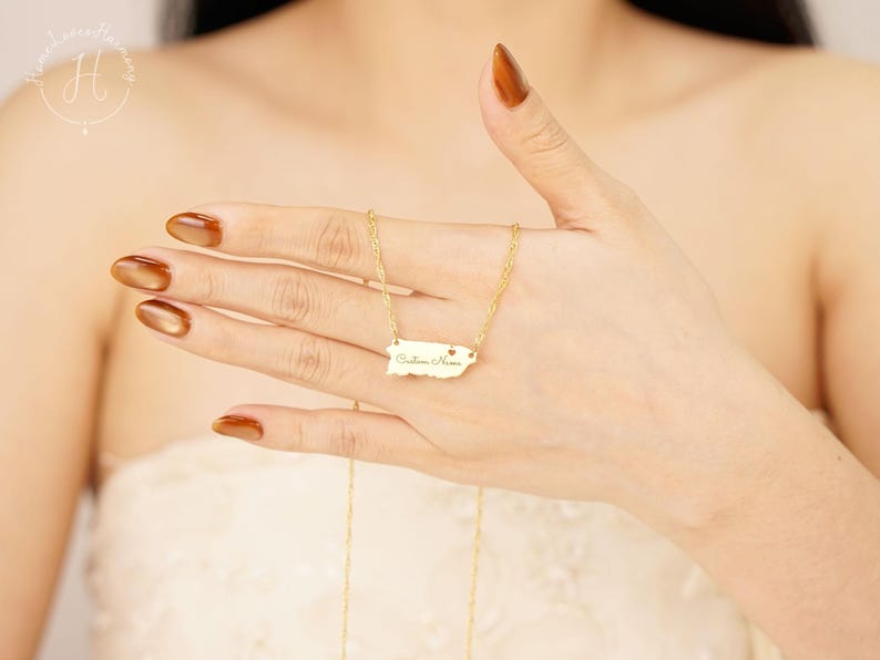 May include: A gold-toned necklace featuring a pendant shaped like the map of Puerto Rico. The pendant includes a small heart cutout and the engraved text Custom Name. The piece is suspended from a delicate gold-toned chain with twisted links.