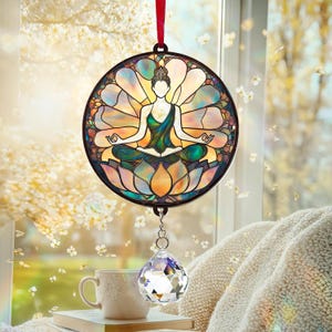 May include: A stained glass window hanging with a crystal prism. The stained glass features a woman in a lotus flower meditating in a colorful mandala design.