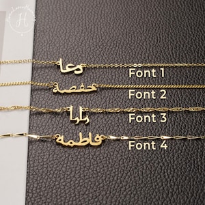 May include: Four gold-toned necklaces featuring Arabic script nameplates, each displayed with a different chain style and font. The labels Font 1, Font 2, Font 3, and Font 4 are printed next to each corresponding necklace on a textured black surface.
