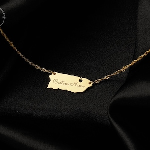 May include: A gold-toned necklace featuring a pendant shaped like the island of Puerto Rico. The pendant includes a small heart cutout and the engraved text "Custom Name" in a cursive script. The pendant is attached to a delicate twisted chain.