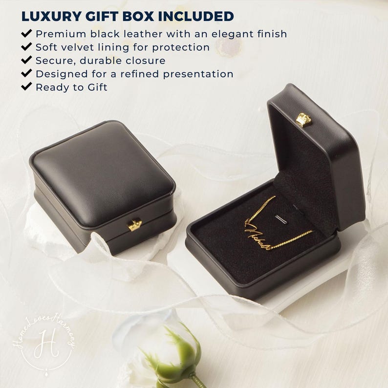 May include: Two black rectangular jewelry boxes with gold-tone latches. One box is closed, and the other is open, revealing a gold-tone chain necklace with a cursive name pendant resting on a black velvet interior lining.