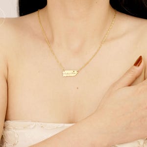 May include: A gold-toned necklace featuring a delicate chain and a small, flat pendant shaped like the island of Puerto Rico. The pendant is engraved with the text 'Culebra, Puerto Rico' and includes a tiny heart symbol near the text.