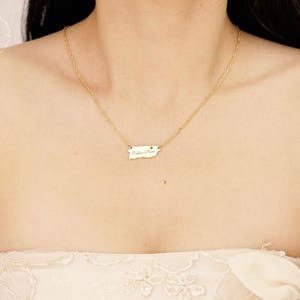 May include: A gold-toned necklace featuring a delicate chain and a small, flat pendant shaped like the island of Puerto Rico. The pendant is engraved with the cursive text "Puerto Rico" and hangs centered on the chain against the collarbone.