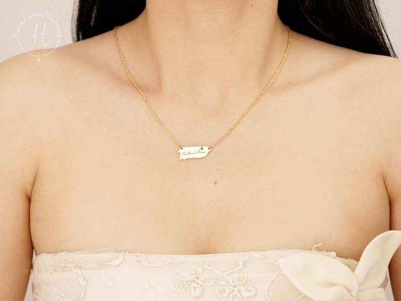 May include: A gold-toned necklace featuring a delicate chain and a small, flat pendant shaped like the island of Puerto Rico. The pendant is engraved with the cursive text "Puerto Rico" and hangs centered on the chain against the collarbone.