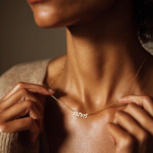 May include: A fine gold necklace with a pendant displaying Thai script. The necklace is worn, with the chain and pendant visible against the skin. The image is well-lit, highlighting the jewelry's details.