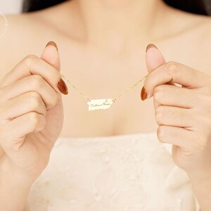 May include: A gold-toned necklace featuring a pendant shaped like the island of Puerto Rico. The pendant is suspended from a delicate gold-toned chain and includes a small, clear, circular accent stone. The surface of the pendant is engraved with the text "Culebra Home" in a cursive script font.