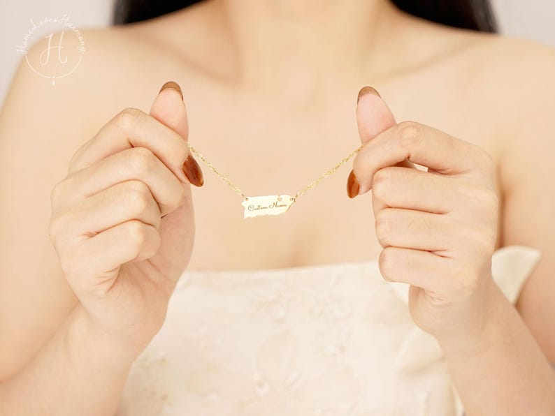 May include: A gold-toned necklace featuring a pendant shaped like the island of Puerto Rico. The pendant is suspended from a delicate gold-toned chain and includes a small, clear, circular accent stone. The surface of the pendant is engraved with the text "Culebra Home" in a cursive script font.