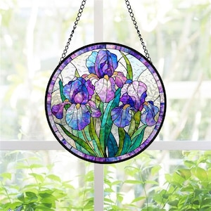 May include: A round stained glass window hanging with a black chain. The window features a vibrant design of purple and blue iris flowers with green leaves. The flowers are set against a clear background, and the window is framed with a black border.