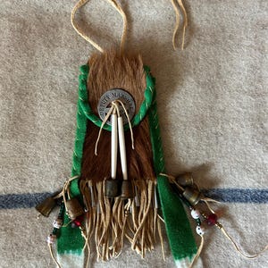 May include: A brown leather pouch with green fringe and a metal badge that reads "Deputy Marshal". The pouch has a white leather strap and is decorated with small bells and beads.