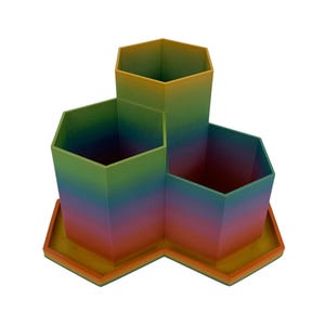 May include: A desk organizer featuring three hexagonal compartments of varying heights arranged on a matching hexagonal base. The object displays a vibrant gradient color transition shifting from yellow at the top to orange, red, purple, blue, and green.