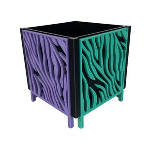 以下が含まれることがあります： 黒い内側と外側のフレームが付いた正方形のプランター。側面は紫とティール色の波のような模様が特徴です。プランターには4つの小さな脚があり、屋内または屋外での使用に適しています。