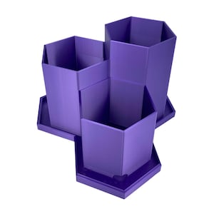 Könnte beinhalten: Ein lila Schreibtisch-Organizer mit drei sechseckigen Fächern. Jedes Fach steht auf einer quadratischen Basis. Der Organizer besteht aus einem soliden, glatten Material und ist für Stifte, Bleistifte oder andere Büroartikel konzipiert.