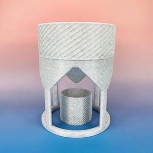 May include: A speckled gray planter with a unique design. The top section has diagonal lines, and the base features a circular design with a cylindrical pot inside. The planter is set against a gradient background of pink and blue.