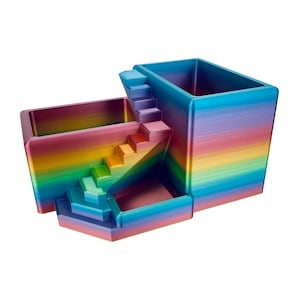 May include: A multi-level desk organiser featuring a vibrant rainbow gradient finish. The structure consists of two rectangular containers connected by a central staircase, creating a tiered design with horizontal colour bands of red, orange, yellow, green, blue, and purple.
