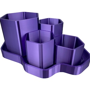 Könnte beinhalten: Ein violetter Schreibtisch-Organizer mit vier sechseckigen Fächern unterschiedlicher Größe, die mit einem Tablett verbunden sind. Der Organizer besteht aus einem soliden Material und hat eine glatte, saubere Oberfläche. Das Design ist modern und funktional.