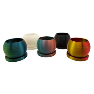 Könnte beinhalten: Fünf kugelförmige Blumentöpfe in verschiedenen Farben, jeweils mit passender runder Untertasse. Die Farben umfassen Teal, Creme, Schwarz und einen Farbverlauf aus Rot, Gelb und Orange. Die Töpfe sind aus glattem Material.