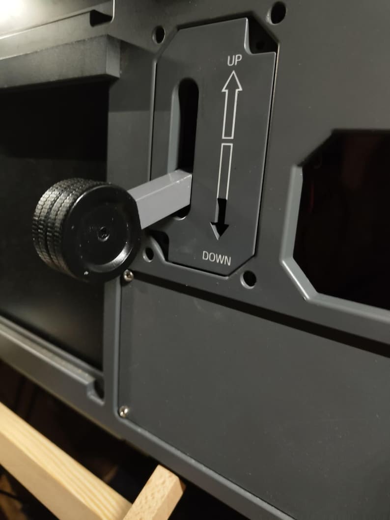May include: Close-up of a dark gray control panel with a black knob and a lever. The panel has the words "UP" and "DOWN" with directional arrows. The knob is textured, and the lever is in the middle position.