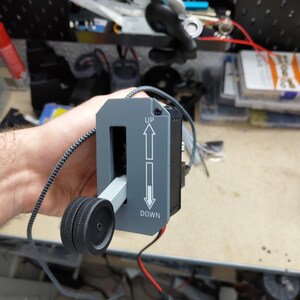 May include: A gray control panel with the words "UP" and "DOWN" and arrows. A black wheel is attached to a lever that moves within the panel. A black and gray cord is attached to the panel.