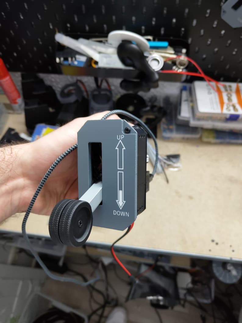 May include: A gray control panel with the words "UP" and "DOWN" and arrows. A black wheel is attached to a lever that moves within the panel. A black and gray cord is attached to the panel.