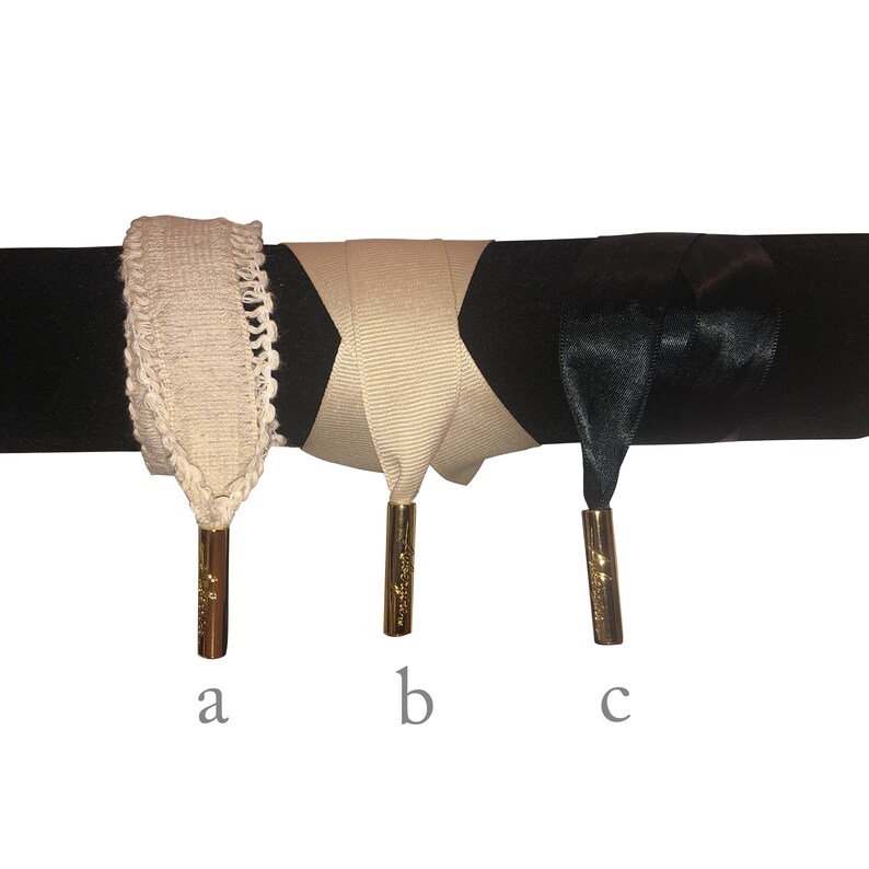 Op de afbeelding: Drie veters met gouden aglets. De veters zijn beige, beige en zwart. De beige veters zijn gemaakt van geweven stof. De zwarte veter is gemaakt van satijn.