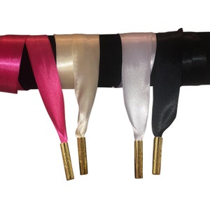 Op de afbeelding: Vier satijnen lint schoenveters met gouden tips. De linten zijn roze, cr&egrave;me, wit en zwart.