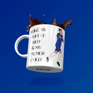 May include: White ceramic mug with a blue and white illustration of a soccer player. The mug has black text that reads "I like my coffee hot & my Palmer cold".