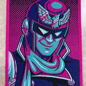 Peut inclure: Un patch brodé rose et bleu représentant un personnage avec un casque bleu et une écharpe rose et bleue. Le personnage a un motif d'aigle bleu et blanc sur le casque. L'arrière-plan est un motif à pois rose et blanc.