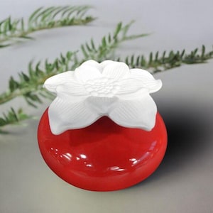 Peut inclure: Un diffuseur en céramique rouge avec une fleur en céramique blanche sur le dessus. La fleur a cinq pétales et un centre avec un motif en relief.