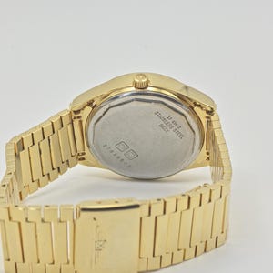 May include: A gold-coloured wristwatch with a stainless steel back. The watch has a rectangular link band and a clasp. The back of the watch has the text "STAINLESS STEEL BACK" and the number "27034503".