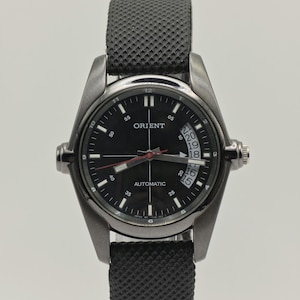 May include: A black Orient automatic wristwatch with a black dial, silver-tone case, and a black fabric strap. The watch features a date display and luminous hands. The watch is a classic design.