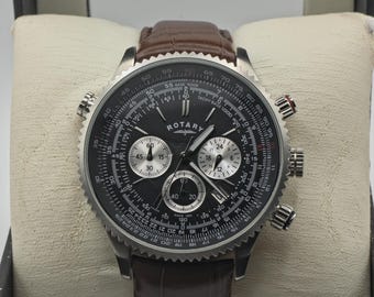 May include: A Rotary chronograph watch with a black dial, silver-tone hands, and three sub-dials. The watch features a stainless steel case with a serrated bezel and a brown leather strap with a textured finish. The dial includes a tachymeter scale.