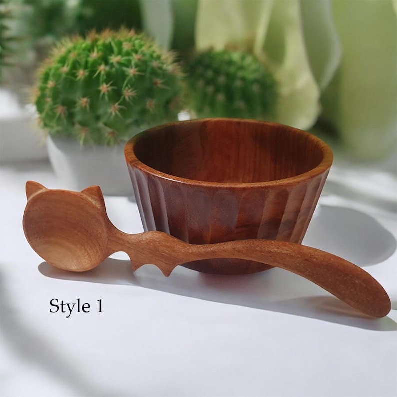 May include: A wooden bowl with a cat-shaped wooden spoon. The bowl is brown and has a fluted design. The spoon is also brown and has a cat's head at the end of the handle. The text "Style 1" is visible below the bowl and spoon.