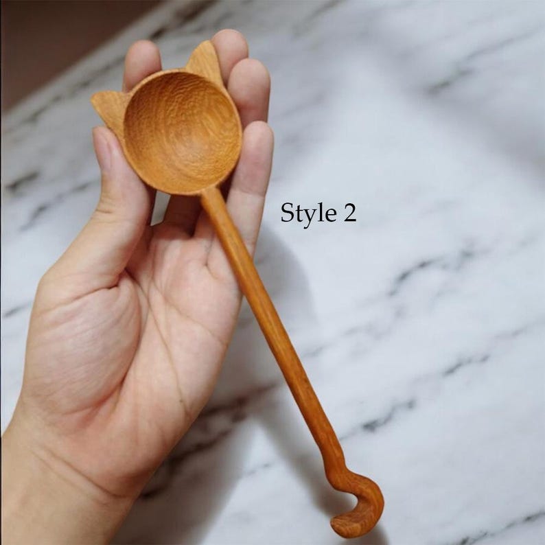May include: A wooden spoon shaped like a cat with a curled tail. The spoon is brown and has a round bowl. The text "Style 2" is visible in the image.