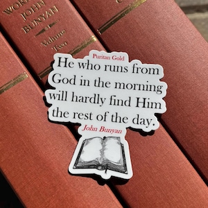 May include: A white sticker with a quote from John Bunyan, "He who runs from God in the morning will hardly find Him the rest of the day." The sticker has a black and white illustration of an open book and the words "Puritan Gold" and "John Bunyan" in red.
