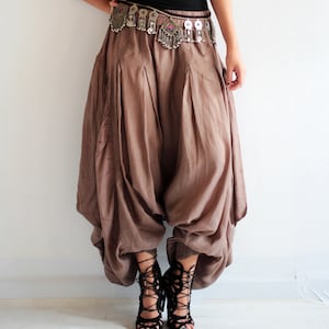 May include: A black tank top paired with brown harem pants. The pants have a gathered, voluminous design. A silver beaded belt and necklace add detail. Black lace-up sandals complete the look. The outfit is bohemian-inspired.